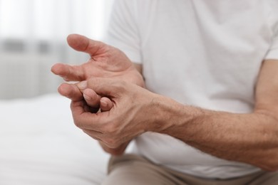 Photo of Arthritis symptoms. Man suffering from pain in hand on bed at home, closeup