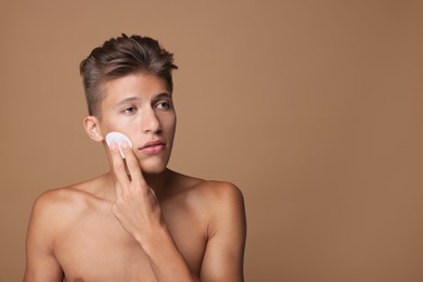 Handsome man cleaning face with cotton pad on beige background, space for text