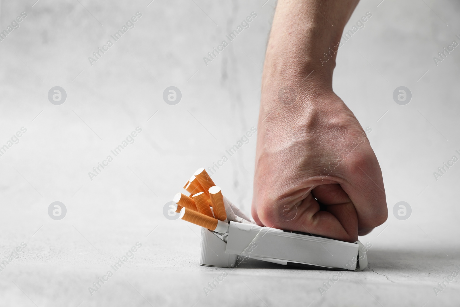 Photo of Stop smoking. Man crushing pack with cigarettes on light background, closeup. Space for text