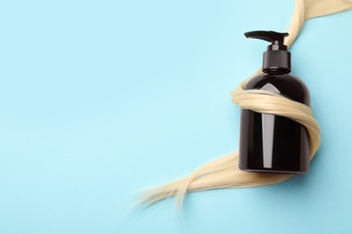 Photo of Shampoo bottle wrapped in lock of hair on light blue background, top view. Space for text