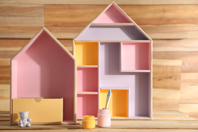 Photo of House shaped shelves, jars of paints and brush on wooden table. Interior elements