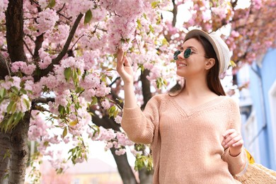 Happy stylish young woman near blossoming sakura tree outdoors. Spring look