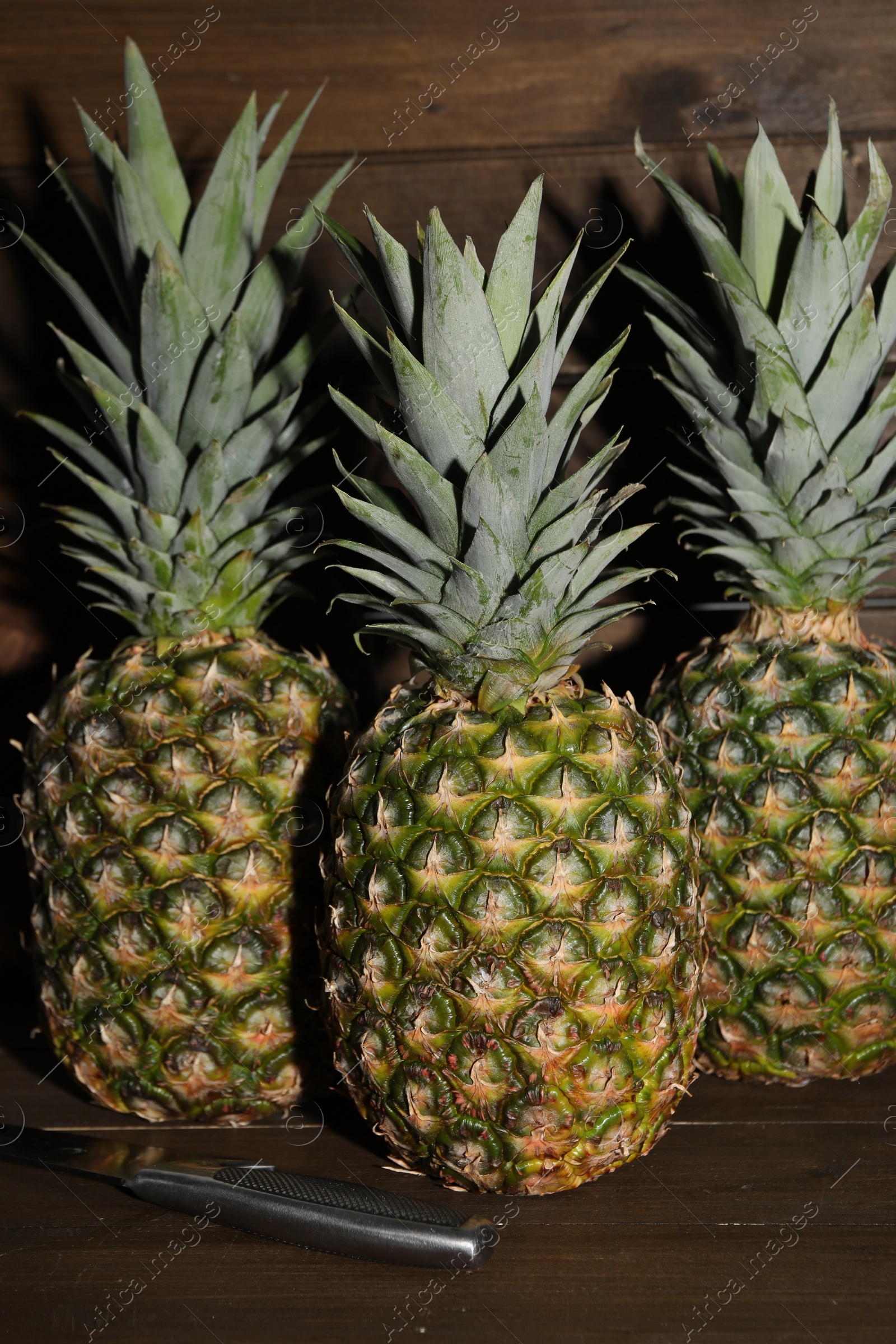 Photo of Whole ripe pineapples and knife on wooden table