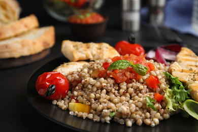 Tasty buckwheat porridge with meat and salad on black table, closeup