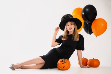 Beautiful woman in witch costume with balloons and pumpkins on white background, space for text. Halloween party