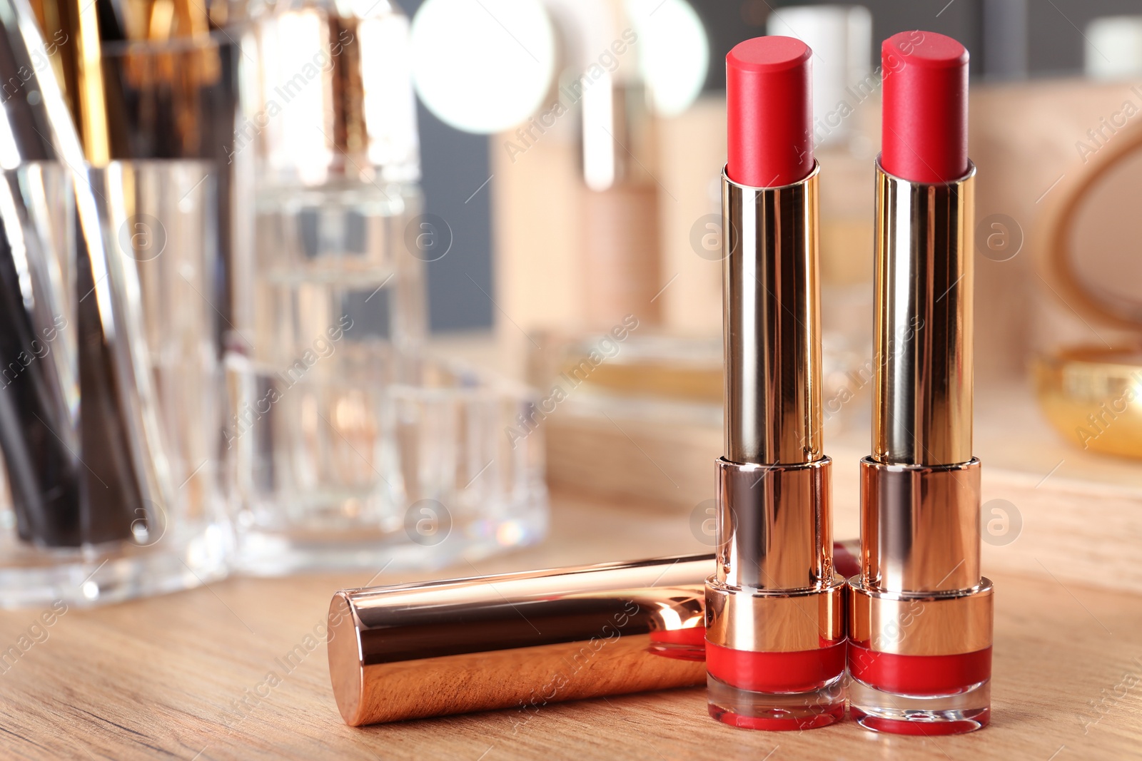 Photo of Open lipsticks in gold tubes on dressing table, space for text