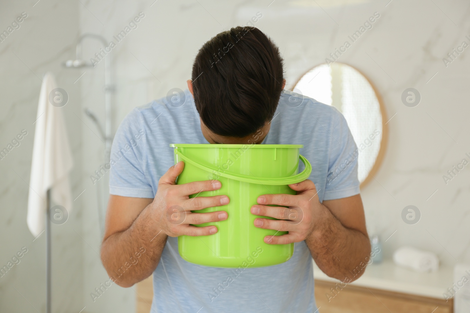 Photo of Man with bucket suffering from nausea in bathroom. Food poisoning