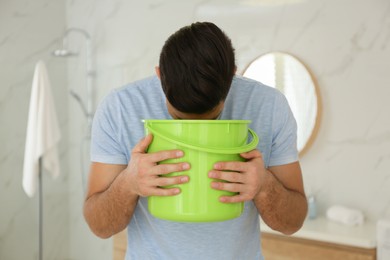 Photo of Man with bucket suffering from nausea in bathroom. Food poisoning