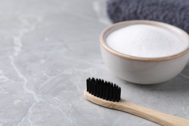 Bamboo toothbrush and bowl of baking soda on light grey table, closeup. Space for text