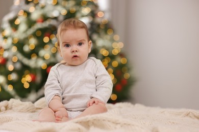 Cute little baby on knitted blanket against blurred festive lights, space for text. Winter holiday