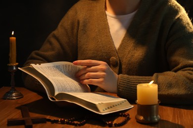 Photo of Woman reading Bible at table with burning candles, closeup