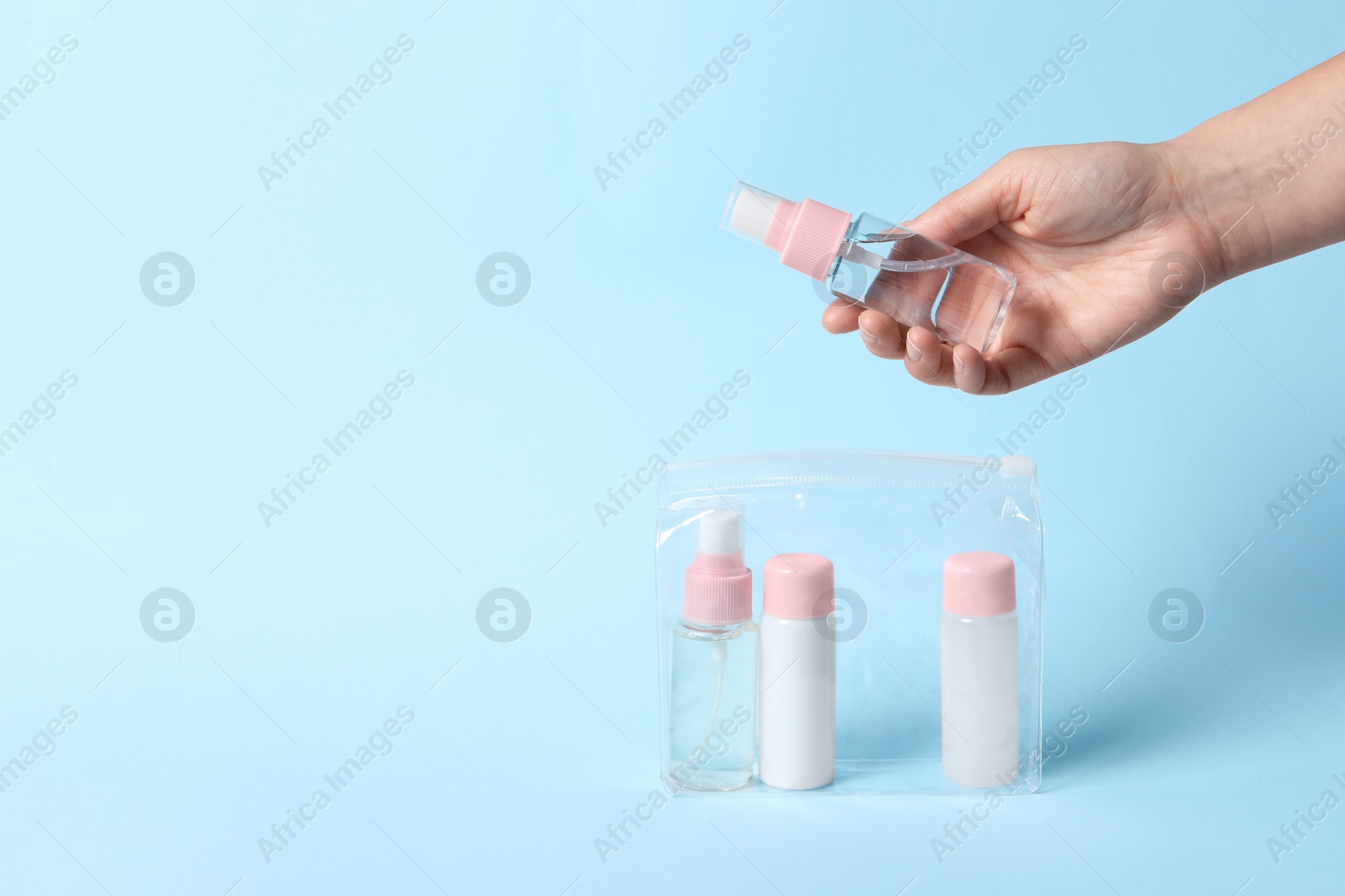 Photo of Cosmetic travel kit. Woman putting small bottle with personal care product into plastic bag against light blue background, closeup. Space for text