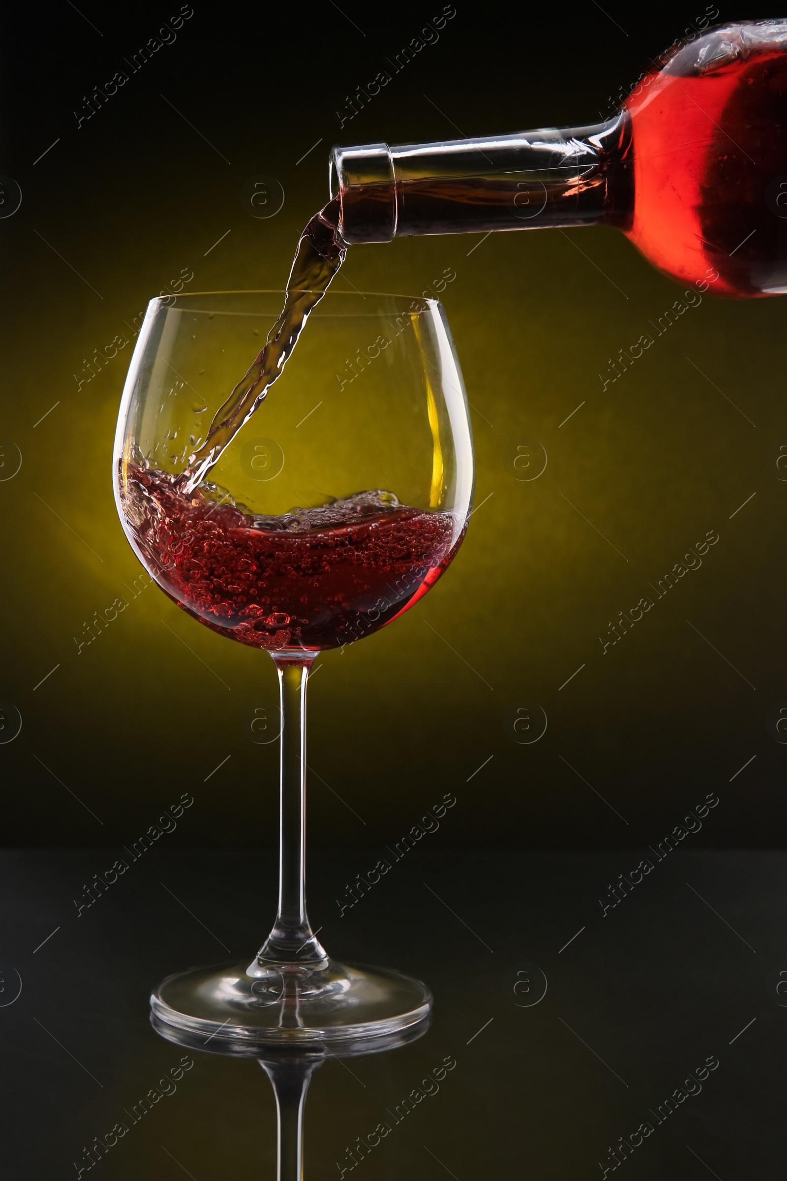 Photo of Pouring red wine from bottle into glass on color background