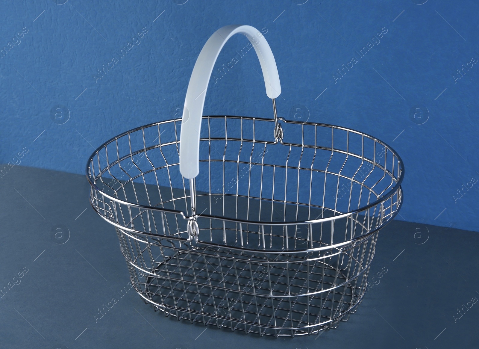 Photo of Empty metal shopping basket on blue background