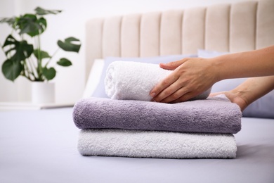 Photo of Woman putting Soft clean terry towels on bed, closeup