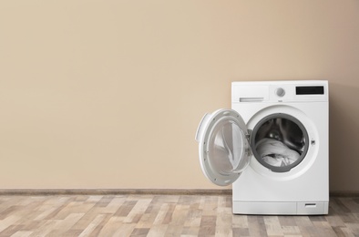 Photo of Modern washing machine with laundry near color wall, space for text