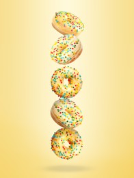 Image of Tasty donuts with sprinkles falling on pastel golden background