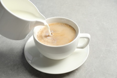 Photo of Pouring milk into cup of hot coffee on grey table