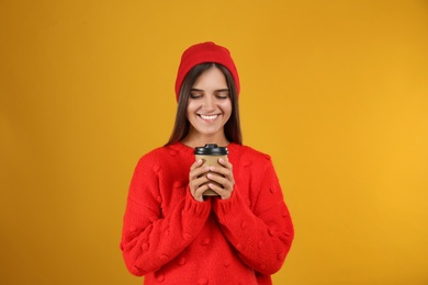 Happy beautiful woman with paper cup of mulled wine on yellow background