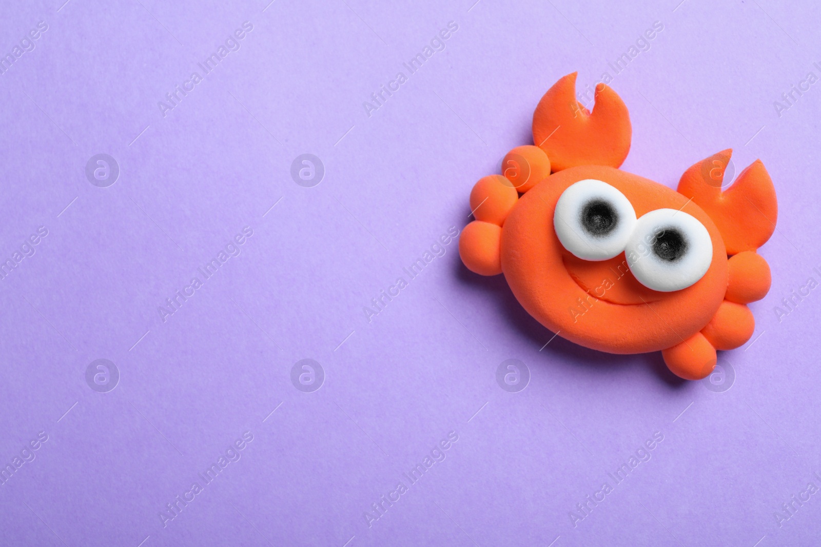 Photo of Colorful crab made from play dough on violet background, top view. Space for text