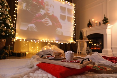 Photo of MYKOLAIV, UKRAINE - DECEMBER 24, 2020: Video projector screen displaying Home Alone movie in room, focus on tray with snack and drink. Cozy winter holidays atmosphere