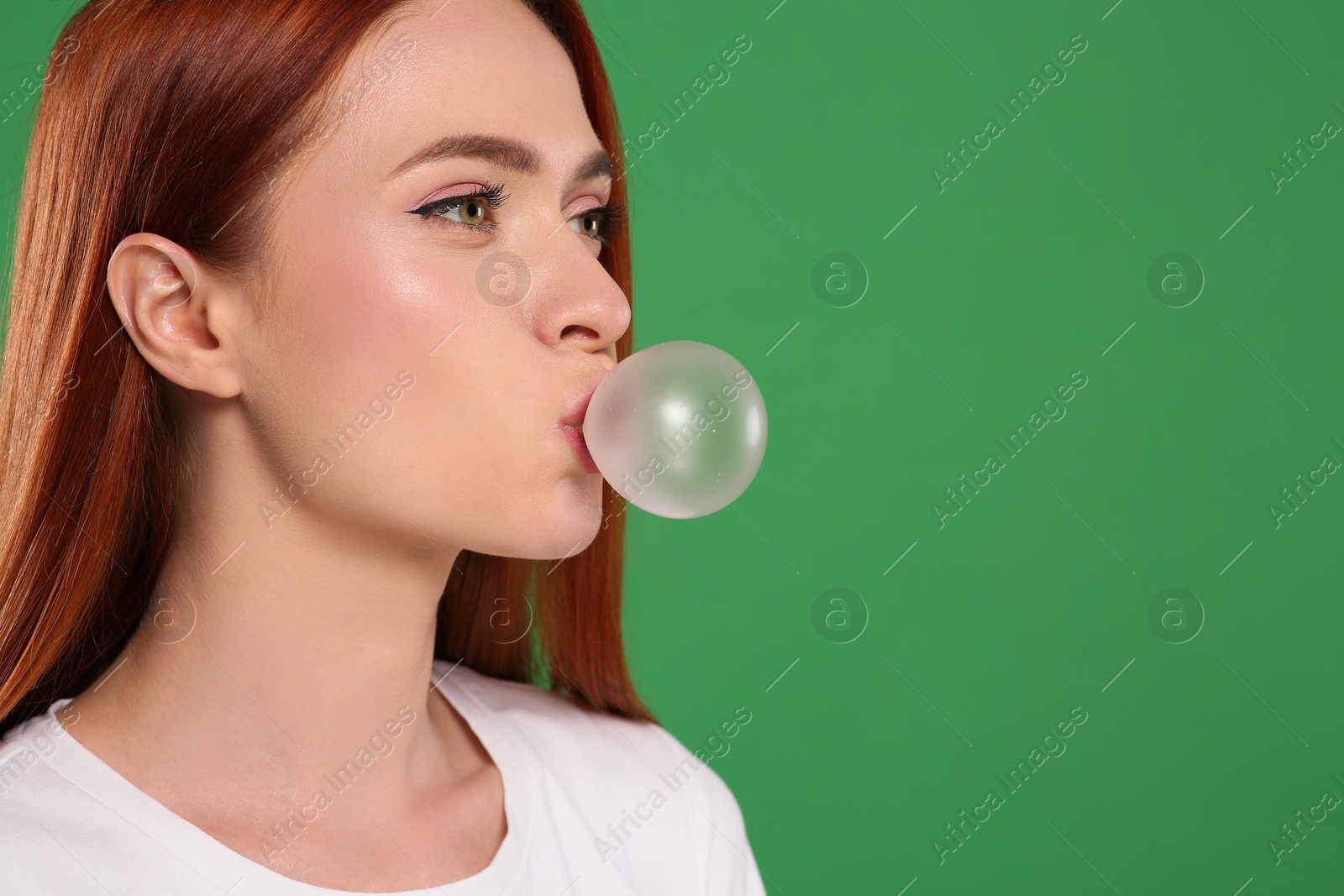 Photo of Beautiful woman blowing bubble gum on green background, space for text