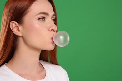 Beautiful woman blowing bubble gum on green background, space for text