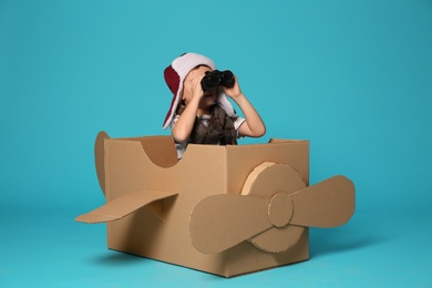 Cute little boy playing with binoculars and cardboard airplane on color background