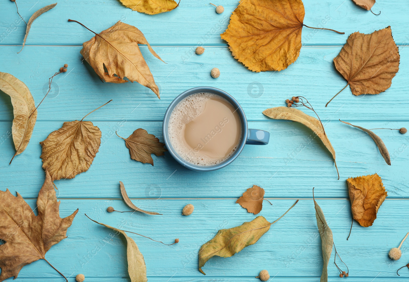 Photo of Cup of hot drink and autumn leaves on light blue wooden table, flat lay. Cozy atmosphere