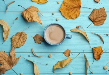 Photo of Cup of hot drink and autumn leaves on light blue wooden table, flat lay. Cozy atmosphere