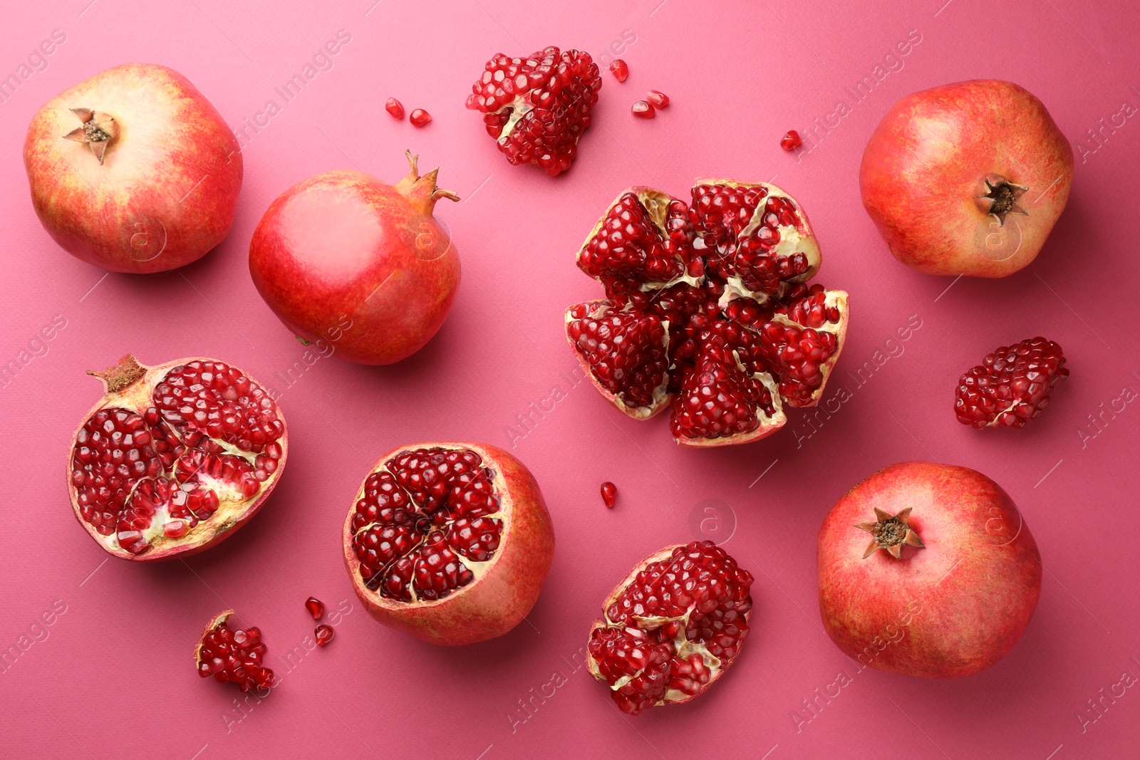 Photo of Whole and cut fresh pomegranates on pink background, flat lay