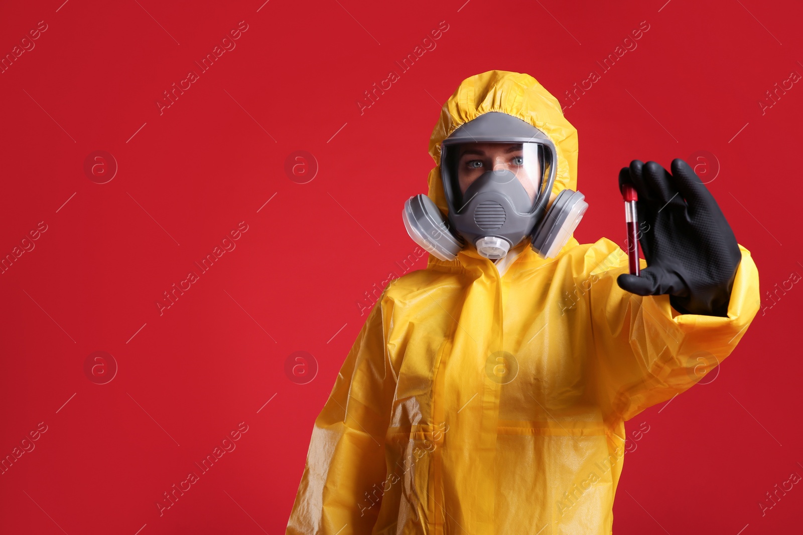 Photo of Woman in chemical protective suit holding test tube of blood sample on red background, space for text. Virus research