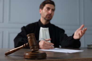 Judge with gavel and papers sitting at wooden table indoors, selective focus