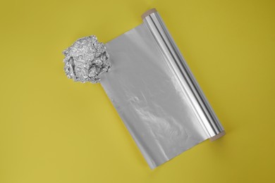 Roll of aluminum foil and crumpled ball on yellow background, top view