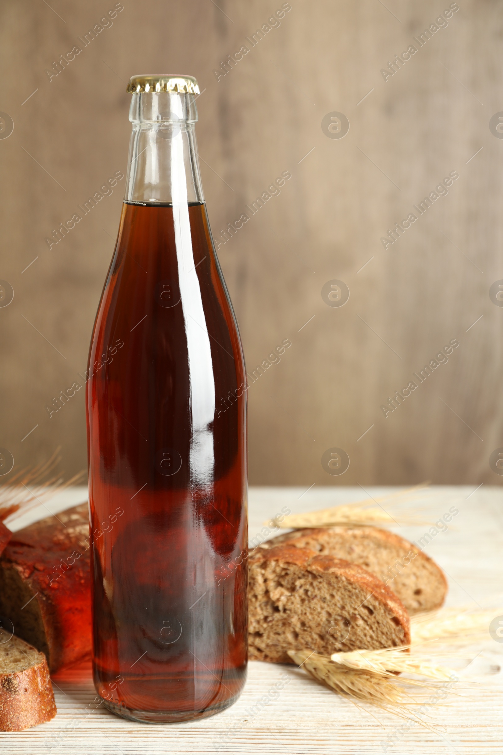 Photo of Bottle of delicious fresh kvass, spikelets and bread on white wooden table