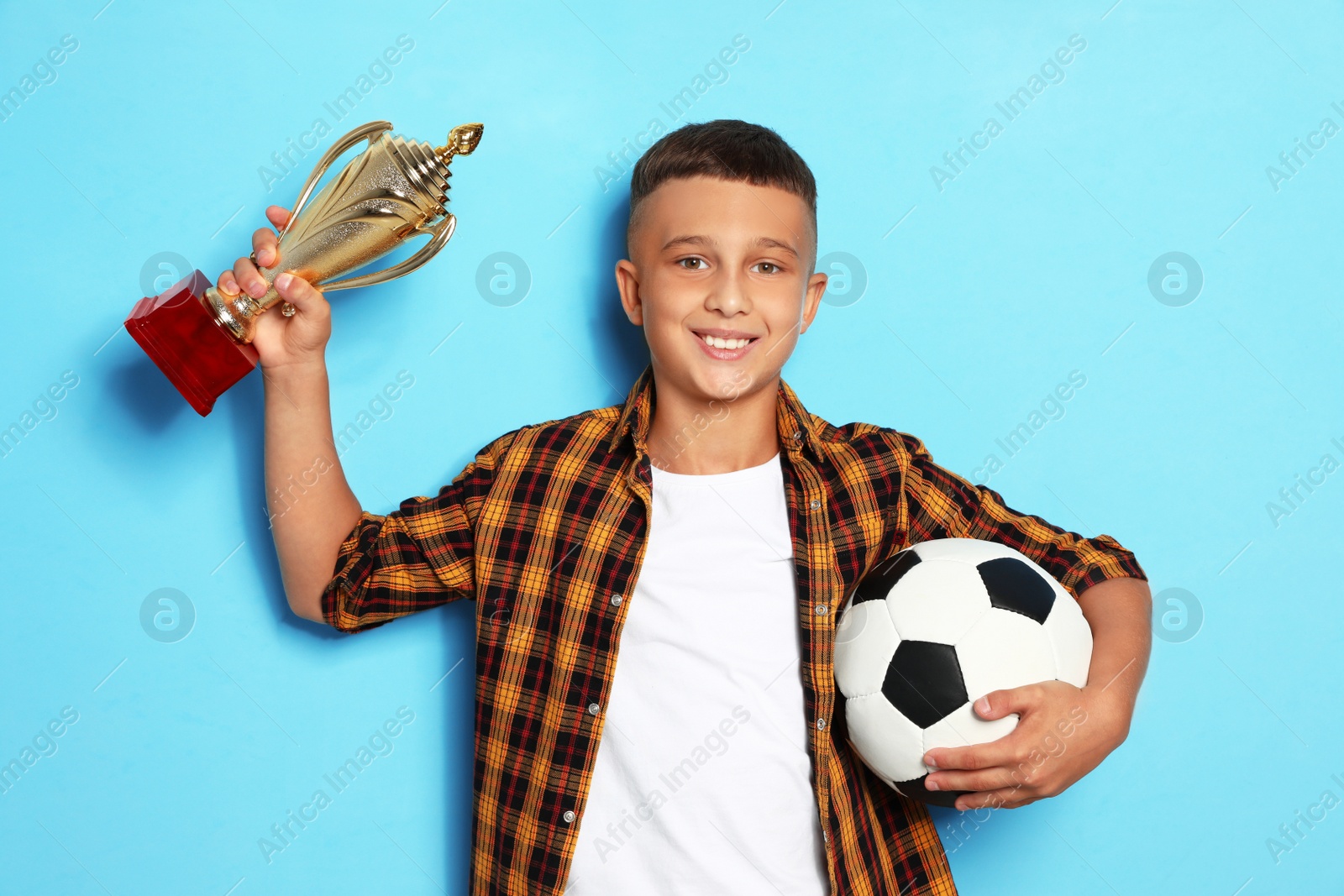 Photo of Happy boy with golden winning cup and soccer ball on blue background
