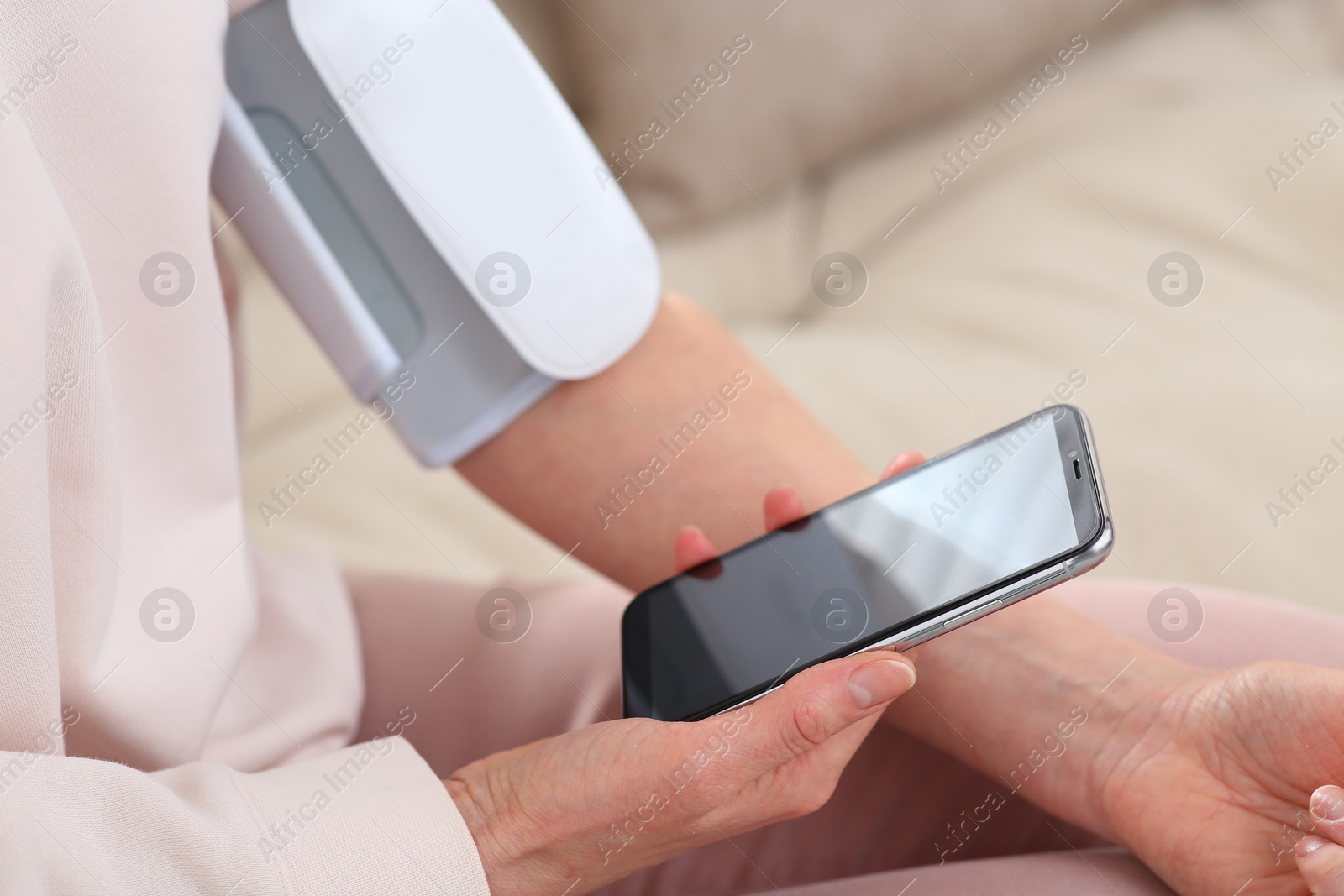 Photo of Woman checking blood pressure with modern monitor and smartphone indoors, closeup