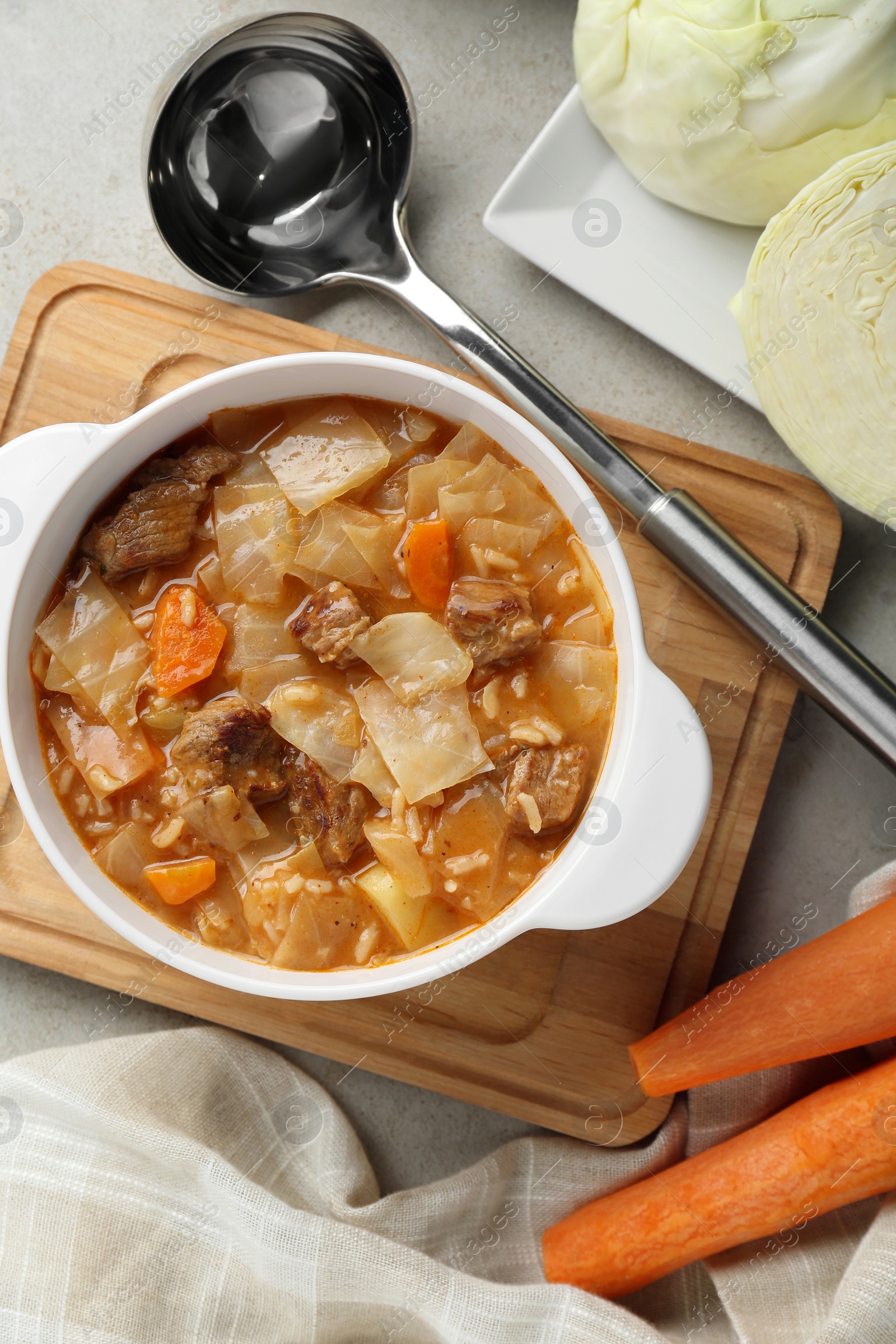 Photo of Tasty cabbage soup and ingredients on light grey textured table, flat lay