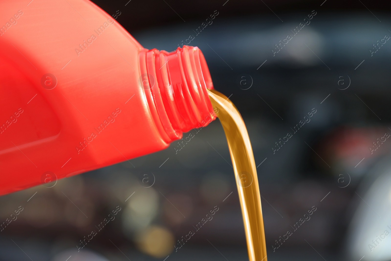 Photo of Pouring motor oil from red container on blurred background, closeup