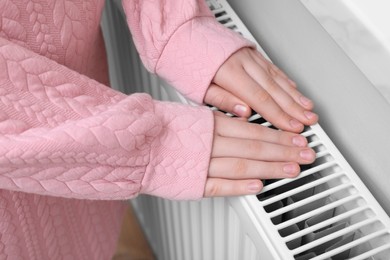 Photo of Girl warming hands on heating radiator indoors, closeup