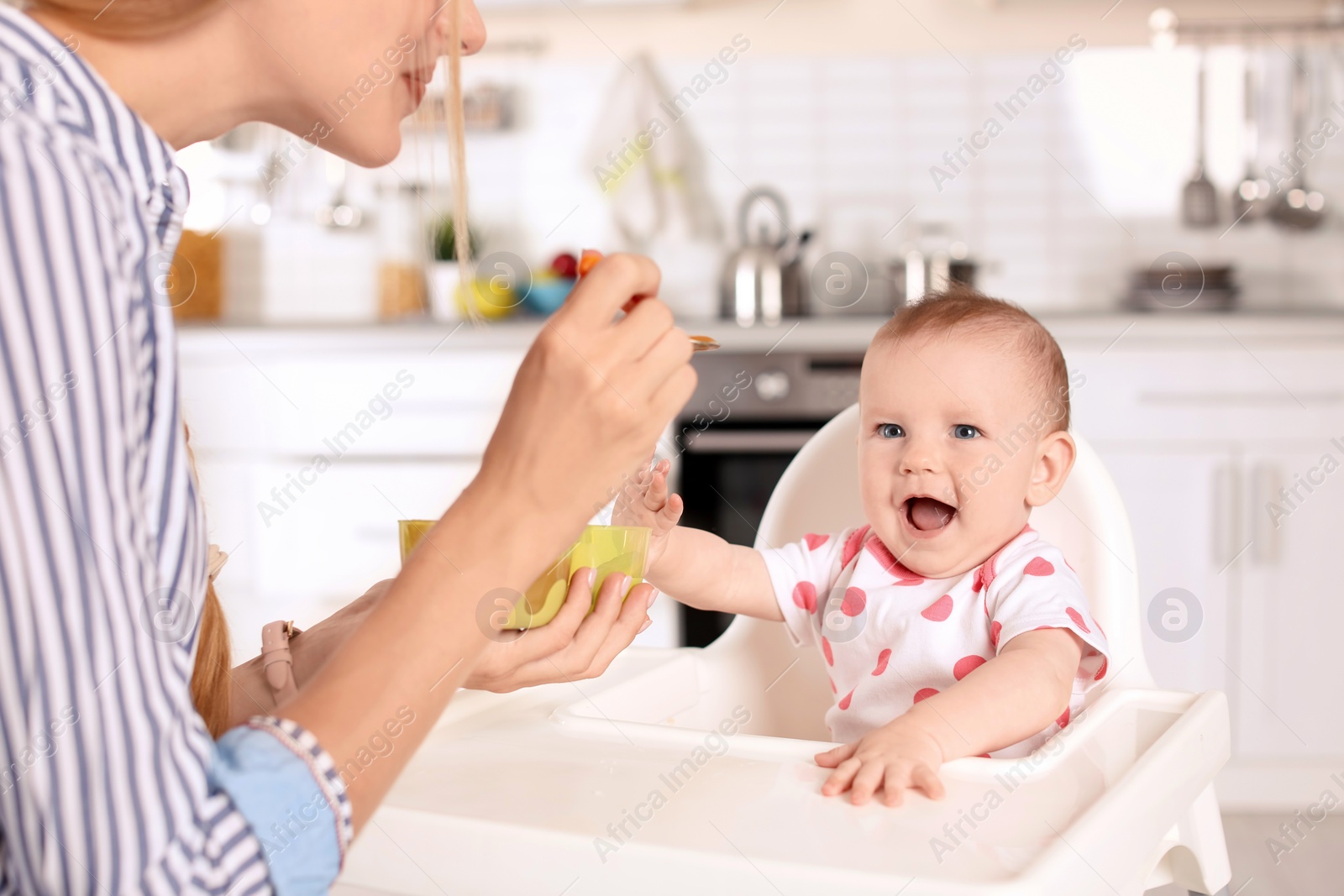 Photo of Woman feeding her child in highchair indoors. Healthy baby food