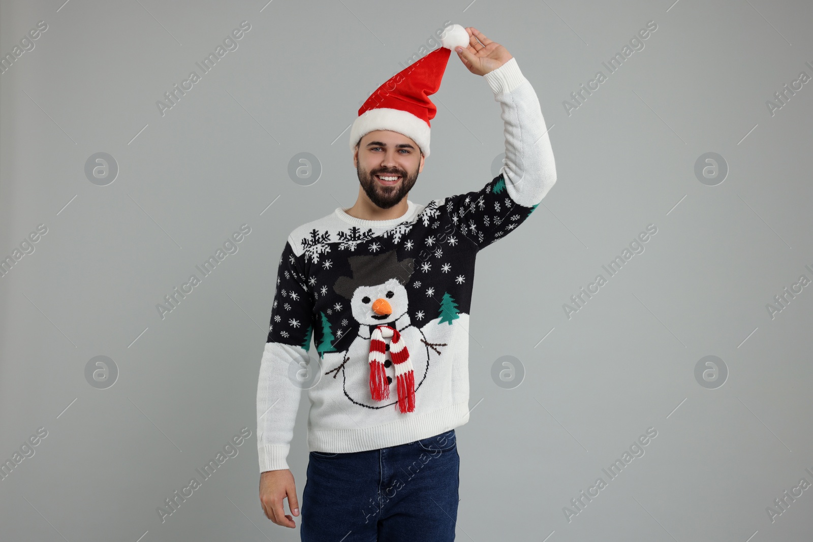 Photo of Happy young man in Christmas sweater and Santa hat on grey background