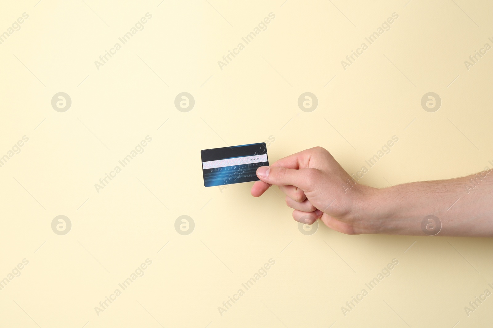 Photo of Man holding credit card on pale yellow background, closeup