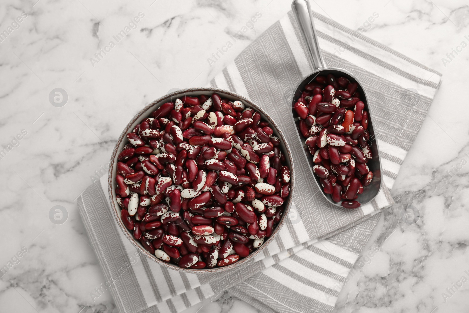 Photo of Bowl and metal scoop with dry kidney beans on white marble table, top view