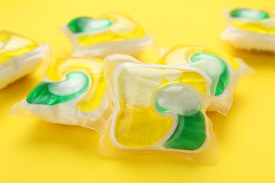 Photo of Many dishwasher detergent pods on yellow background, closeup