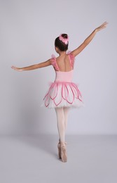 Photo of Beautifully dressed little ballerina dancing on grey background, back view