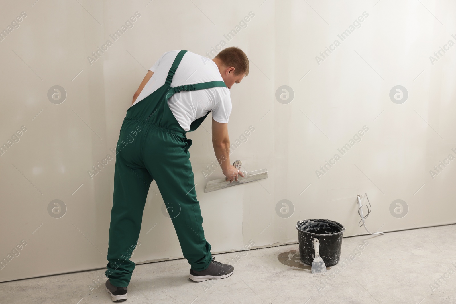 Photo of Professional worker plastering wall with putty knife indoors