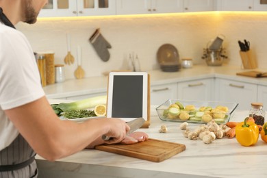 Photo of Man cutting chicken fillet while watching online cooking course via tablet in kitchen, closeup