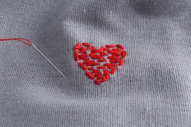 Embroidered red heart and needle on gray cloth, above view