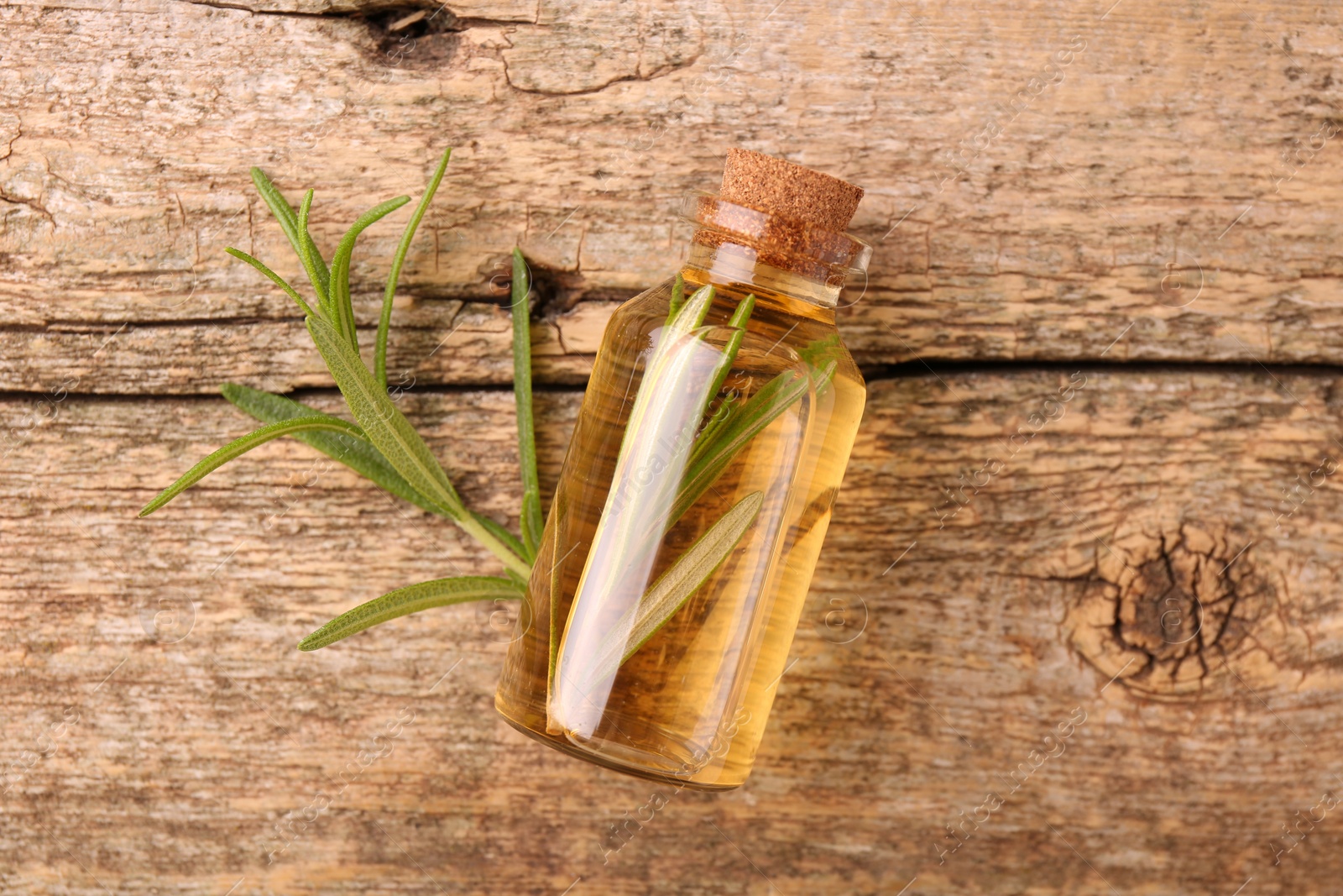 Photo of Aromatic essential oil in bottle and rosemary on wooden table, top view